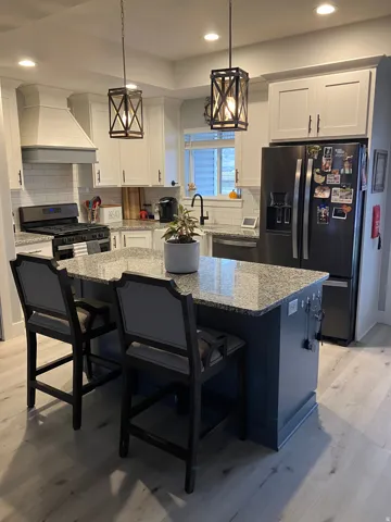 Kitchen featuring a central island with a granite-style countertop, stainless steel appliances, white subway tile backsplash, white shaker-style cabinetry, and recessed lighting