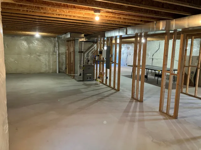 Unfinished lower level with wood framing, exposed ceiling joists, and concrete flooring