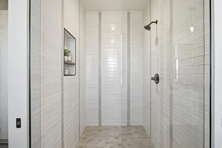 Walk-in shower featuring glass enclosure, built-in recessed shelf, dark bronze fixtures, and pebble-style floor tiling