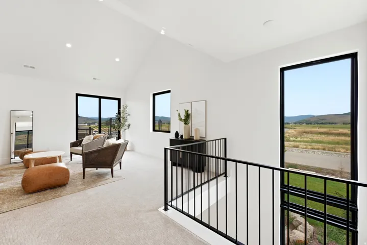 Vaulted ceiling, recessed lighting, black framed windows, black metal railing, and light-colored carpeting