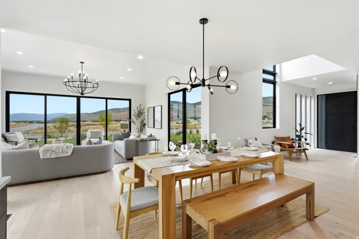 Open concept living area featuring light wood-finish flooring, a contemporary dining chandelier, large format windows, a prominent skylight, and a modern entry door