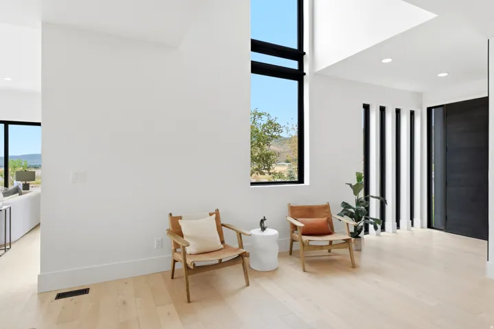 Hardwood flooring, high ceilings, tall windows with black frames, white walls, and a substantial dark entry door