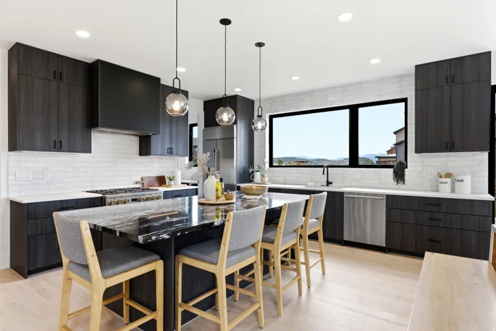 Modern kitchen featuring dark wood-finish cabinetry, a large black island with a polished countertop, stainless steel appliances, and light wood-finish flooring
