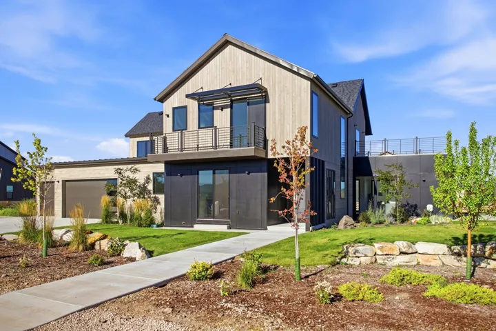 Modern architectural design featuring vertical wood siding, a second-story balcony with metal railing, an attached garage, and a landscaped yard with a concrete pathway