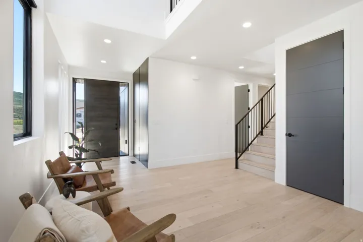 Expansive entryway with light wood-finish flooring, recessed lighting, and a modern dark-paneled door