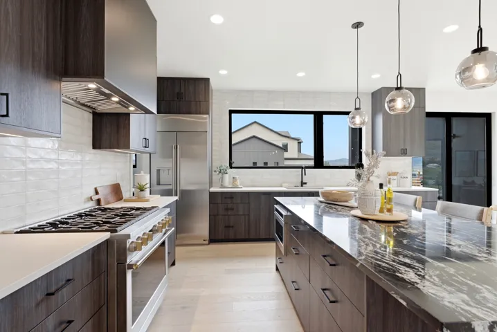 Modern kitchen featuring dark wood-finish cabinetry, stainless steel appliances, a gas range with a professional-grade hood, a large island with a substantial countertop, and pendant lighting
