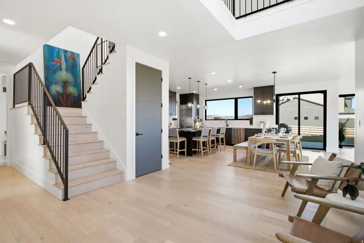 Hardwood flooring extends throughout this open-concept layout, featuring a contemporary kitchen with an island, a distinct dining area, and a staircase with metal railings