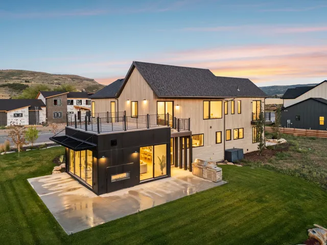 Modern architecture featuring light wood siding, a dark shingle roof, a concrete patio, a built-in outdoor kitchen, and an upper-level balcony with metal railings