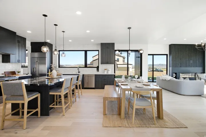 Spacious open-concept living area featuring light wood-finish flooring, a large kitchen island with a stone countertop, dark cabinetry, and multiple pendant light fixtures