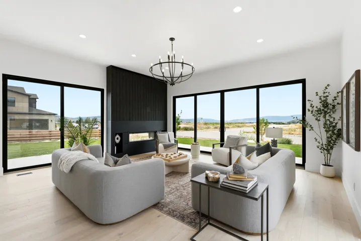 Spacious living area featuring expansive glass sliding doors, a linear fireplace with a dark wood accent wall, a prominent chandelier, and recessed lighting