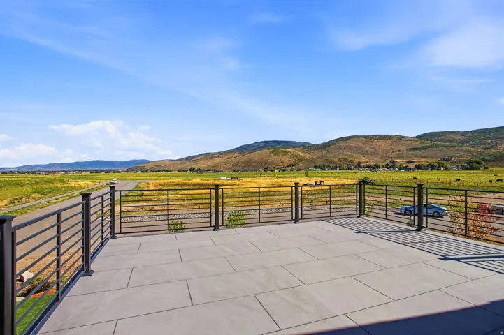 Expansive outdoor deck featuring large format tile flooring, black metal railing, and distant mountain scenery