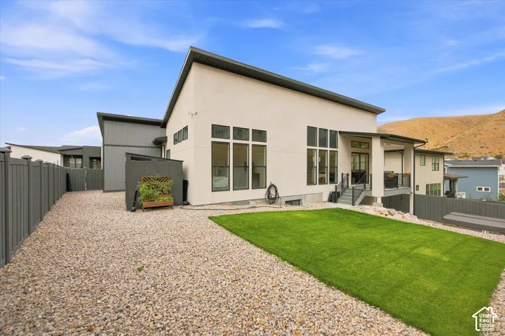 Contemporary architecture featuring an expansive gravel area, a manicured lawn, a covered outdoor deck, and large windows