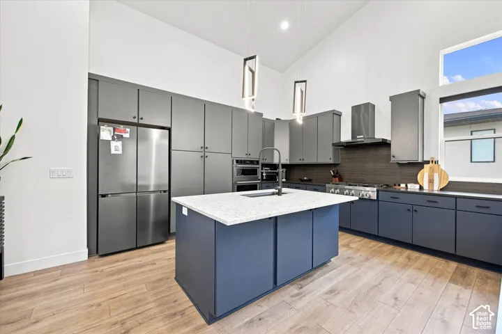 Kitchen with vaulted ceilings, recessed lighting, wood-finish flooring, an oversized island with a light-colored countertop, and integrated stainless steel appliances