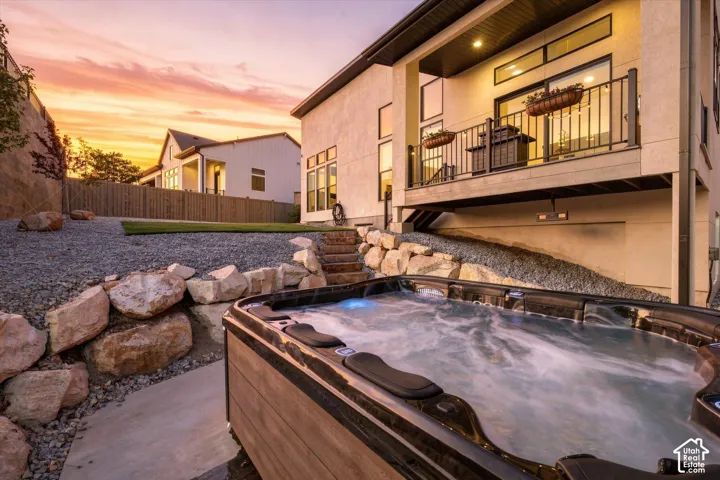 Outdoor spa with wood-finish siding, rock-lined landscaping, concrete pathway, and an elevated balcony with a metal railing