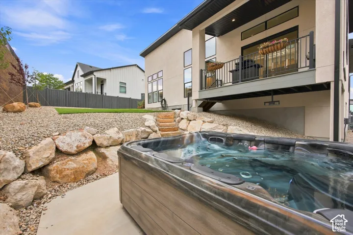 Outdoor spa with concrete surround, multi-level landscaping with decorative rocks, and a raised exterior balcony with dark railings