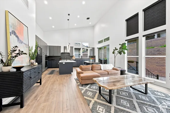Open-concept living space featuring soaring ceilings with recessed lighting, wide-plank wood-finish flooring throughout, and expansive windows with black-framed glass panes