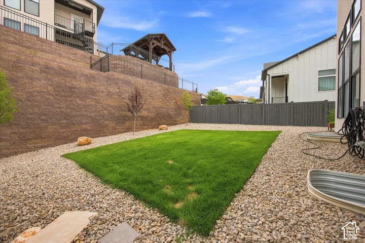 Manicured lawn area with surrounding gravel landscaping, a retaining wall, and an elevated wood gazebo