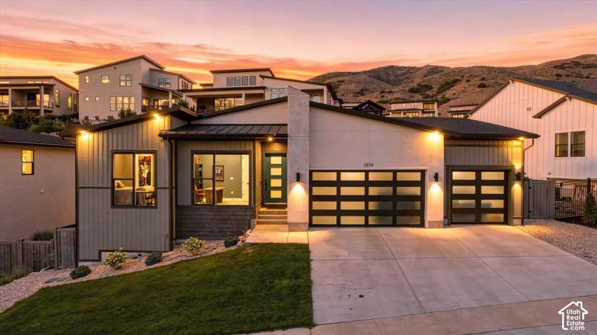 Modern exterior with mixed material siding, illuminated entry, and two garage doors with frosted glass panels