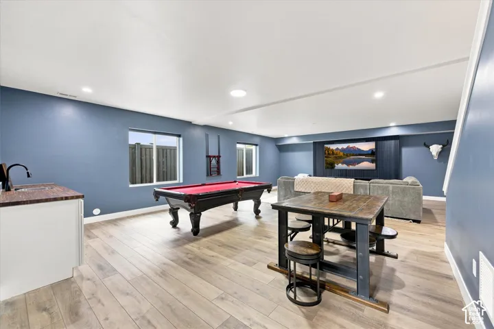 Spacious entertainment area featuring wood-finish flooring, recessed lighting, and a built-in wet bar with a dark countertop