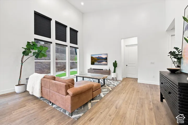 Vaulted ceiling, wood-finish flooring, large windows with roller shades, white walls, and a paneled interior door