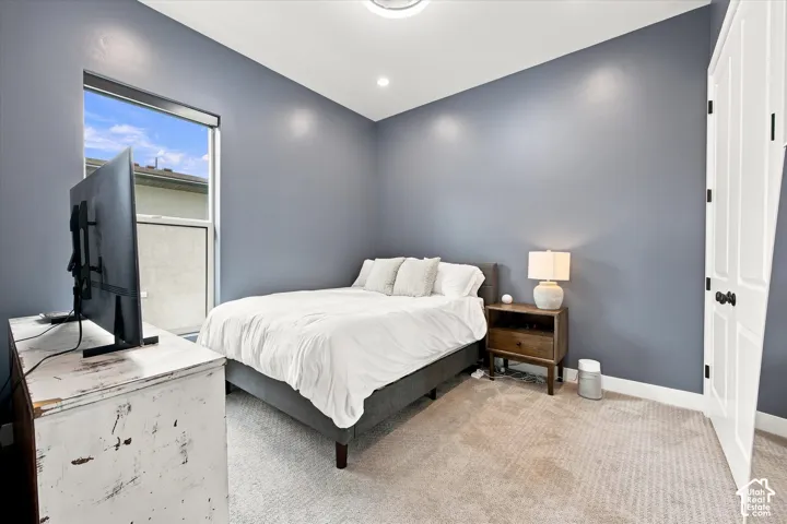 Window with white frame, recessed lighting, wall-mounted light fixture, paneled door with black hardware, and gray carpet flooring