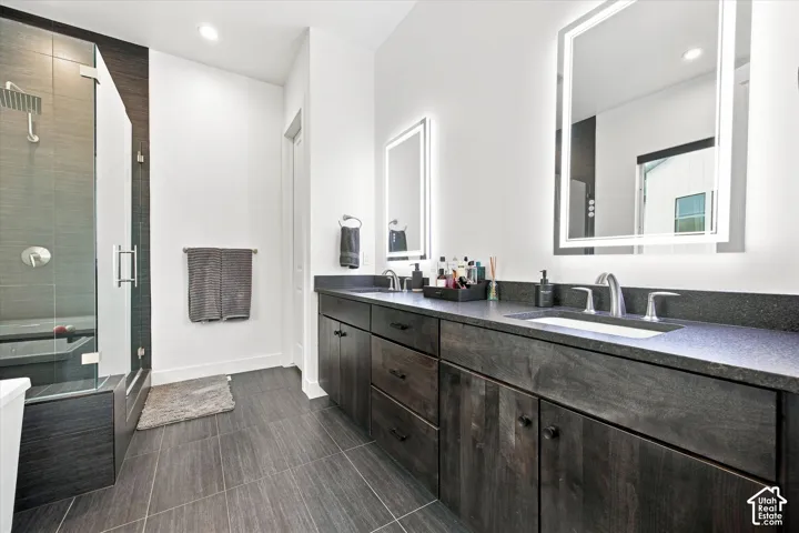 Dual vanity with dark wood-finish cabinetry, illuminated mirrors, and a dark stone countertop