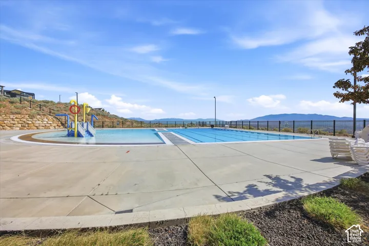 Expansive outdoor pool area featuring a large swimming pool, an adjacent shallow pool with water play structure, and concrete decking