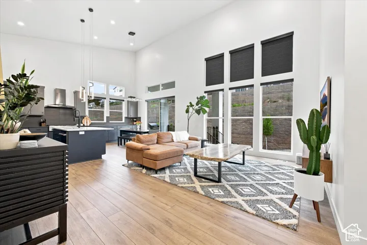 Expansive open-concept living area with soaring ceilings, wood-finish flooring, a modern kitchen island, large window array, and recessed lighting