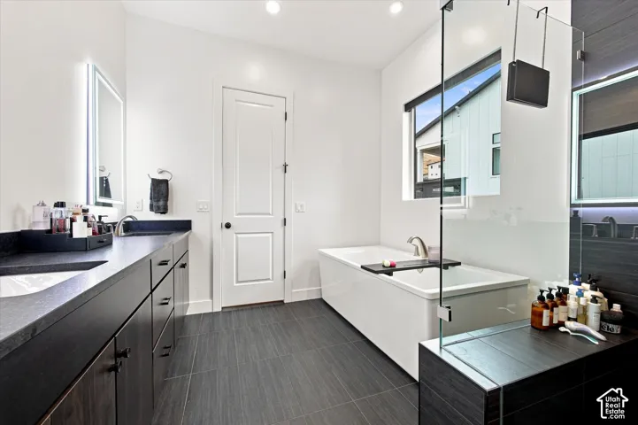 Elongated soaking tub, frameless glass shower enclosure, dark wood-finish vanity with countertop, rectangular window, and large format floor tiling