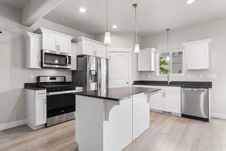 Kitchen featuring stainless steel appliances, white cabinetry, dark stone countertops, a central island, and wood-finish flooring