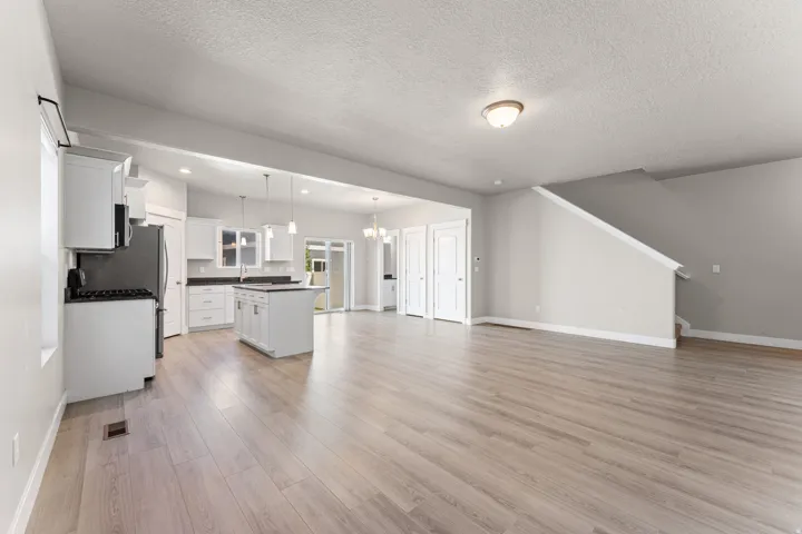 Open-concept living space featuring wood-finish flooring, a contemporary kitchen with white cabinetry, a kitchen island, and stainless steel appliances