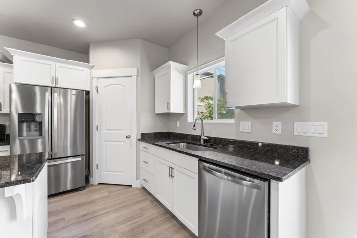 White shaker cabinetry with dark stone countertops, stainless steel appliances, and wood-finish flooring