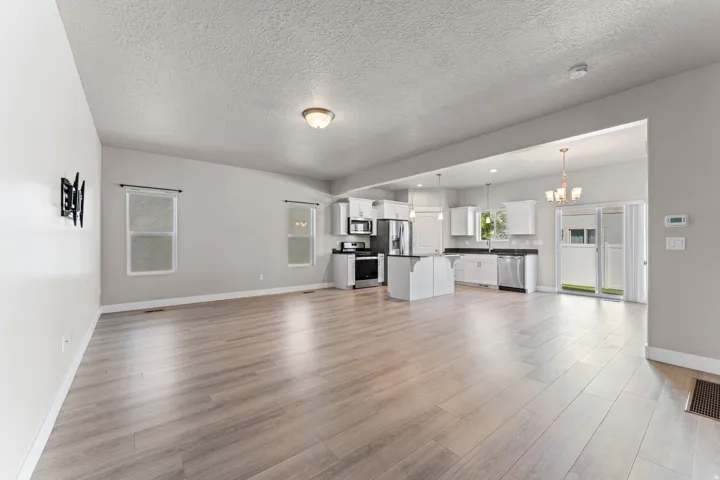 Open-concept living area featuring wood-finish flooring, recessed lighting, white cabinetry, dark countertops, and stainless steel appliances