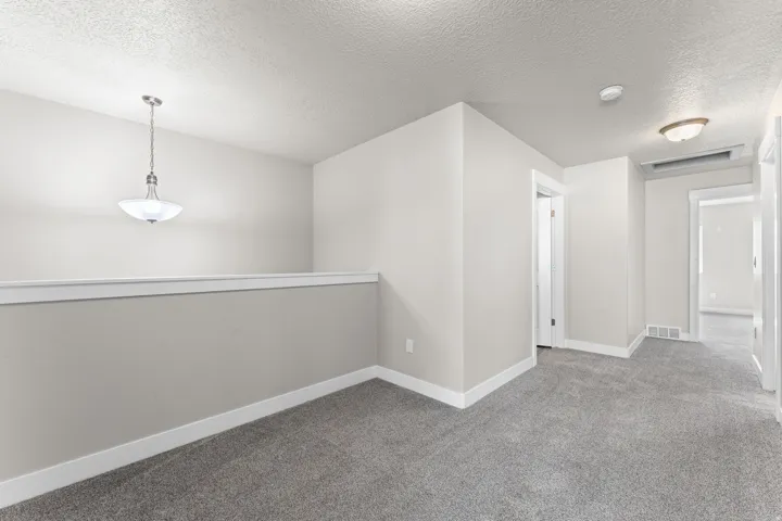 Open loft area with gray carpeting, white trim, and a contemporary pendant light fixture