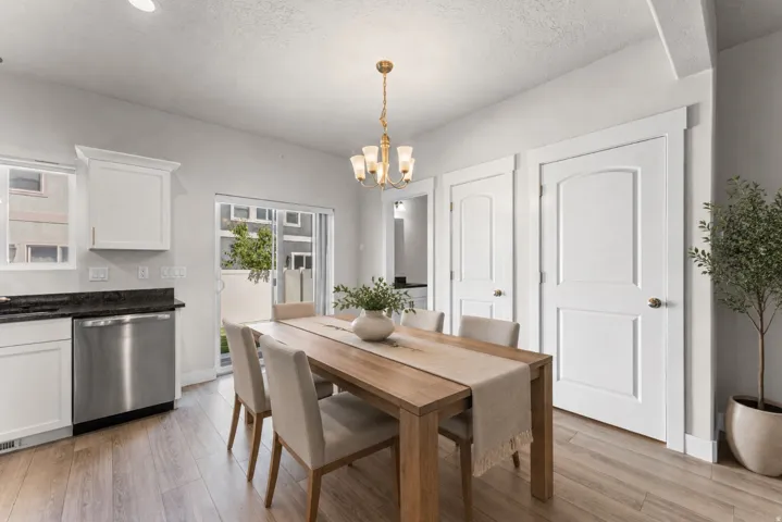 Wood-finish flooring, white cabinetry, dark stone countertops, stainless steel dishwasher, and a brass chandelier