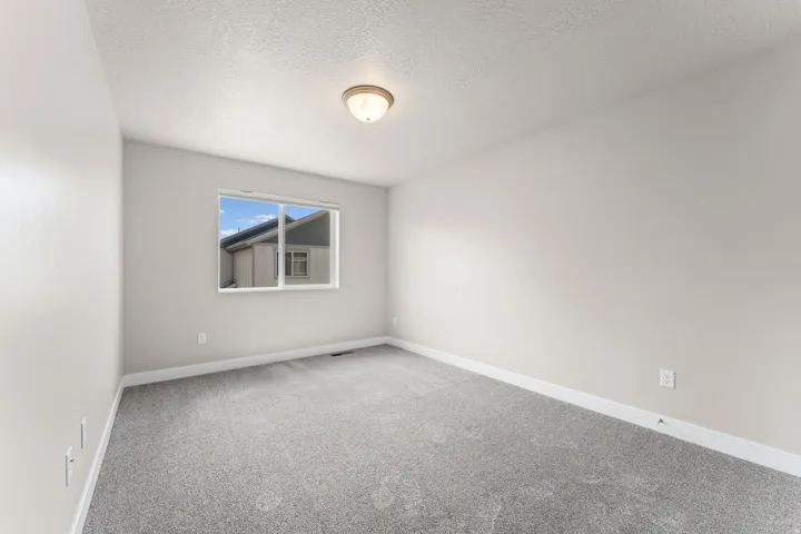 Neutral wall paint, textured ceiling, gray carpeting, a single window, and a flush-mount ceiling light