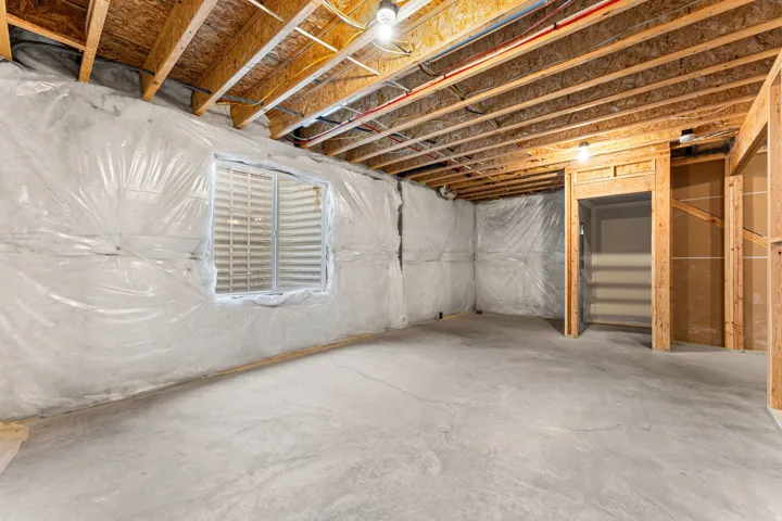 Unfinished basement featuring exposed wood joists, concrete flooring, a window, and framed doorways