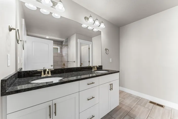 Spa-inspired double vanity bathroom featuring white shaker-style cabinetry, black stone countertops with dual rectangular sinks, polished nickel hardware, and contemporary sconce lighting