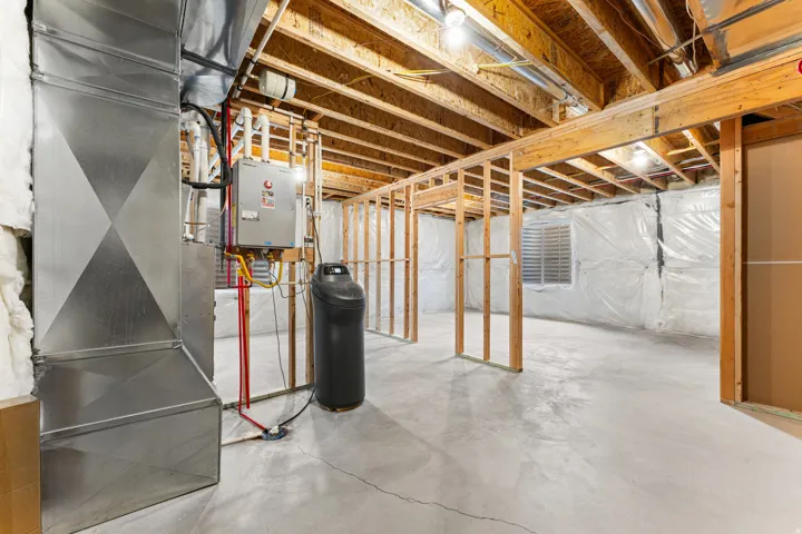 Unfinished basement with exposed wooden joists, concrete flooring, and perimeter wall insulation