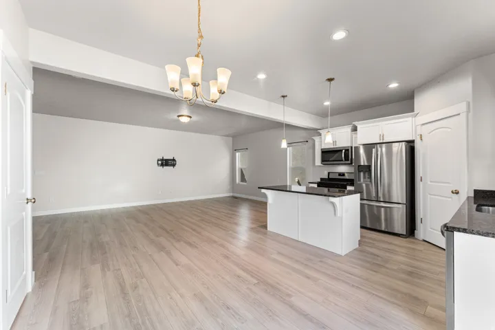 Open-concept living space with wood-finish flooring, white cabinetry, stainless steel appliances, a kitchen island, and a decorative chandelier
