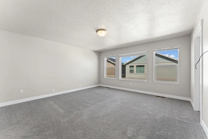 Spacious interior featuring three windows, neutral wall tones, gray carpeting, and a ceiling-mounted light fixture