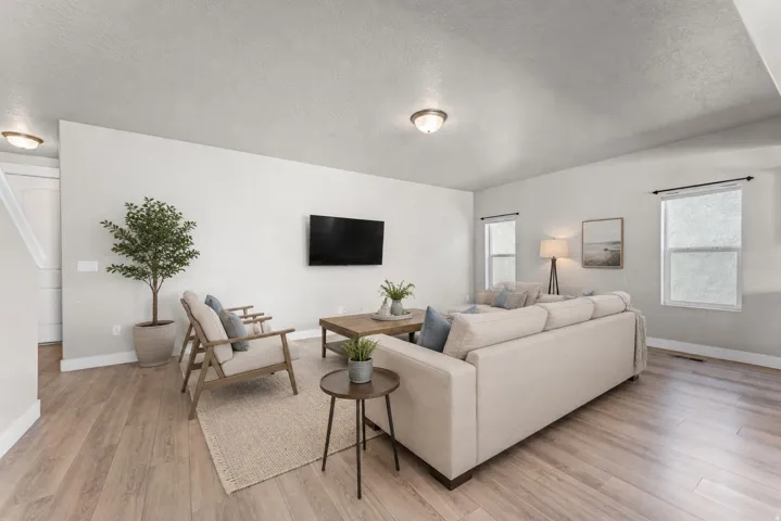 Spacious living area featuring wood-finish flooring, light-toned walls, multiple windows, and recessed ceiling lighting