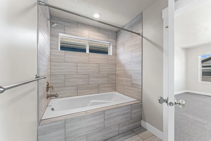 Bathtub with full wall tile surround, bronze fixtures, and a recessed window