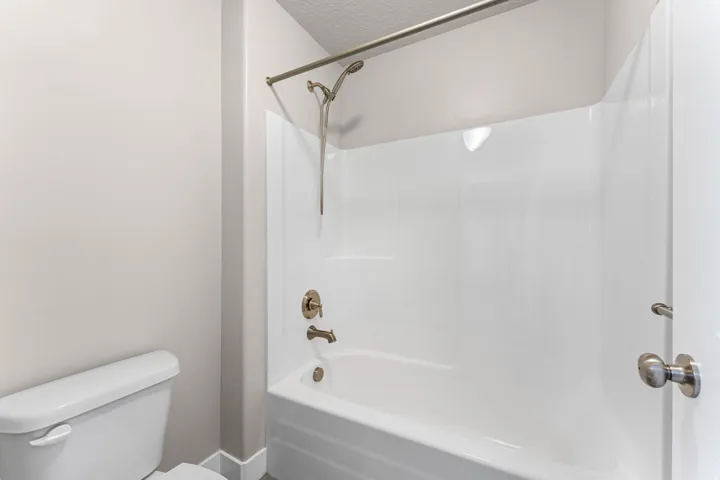 White bathtub with integrated shower, brushed bronze fixtures, and a curved shower rod