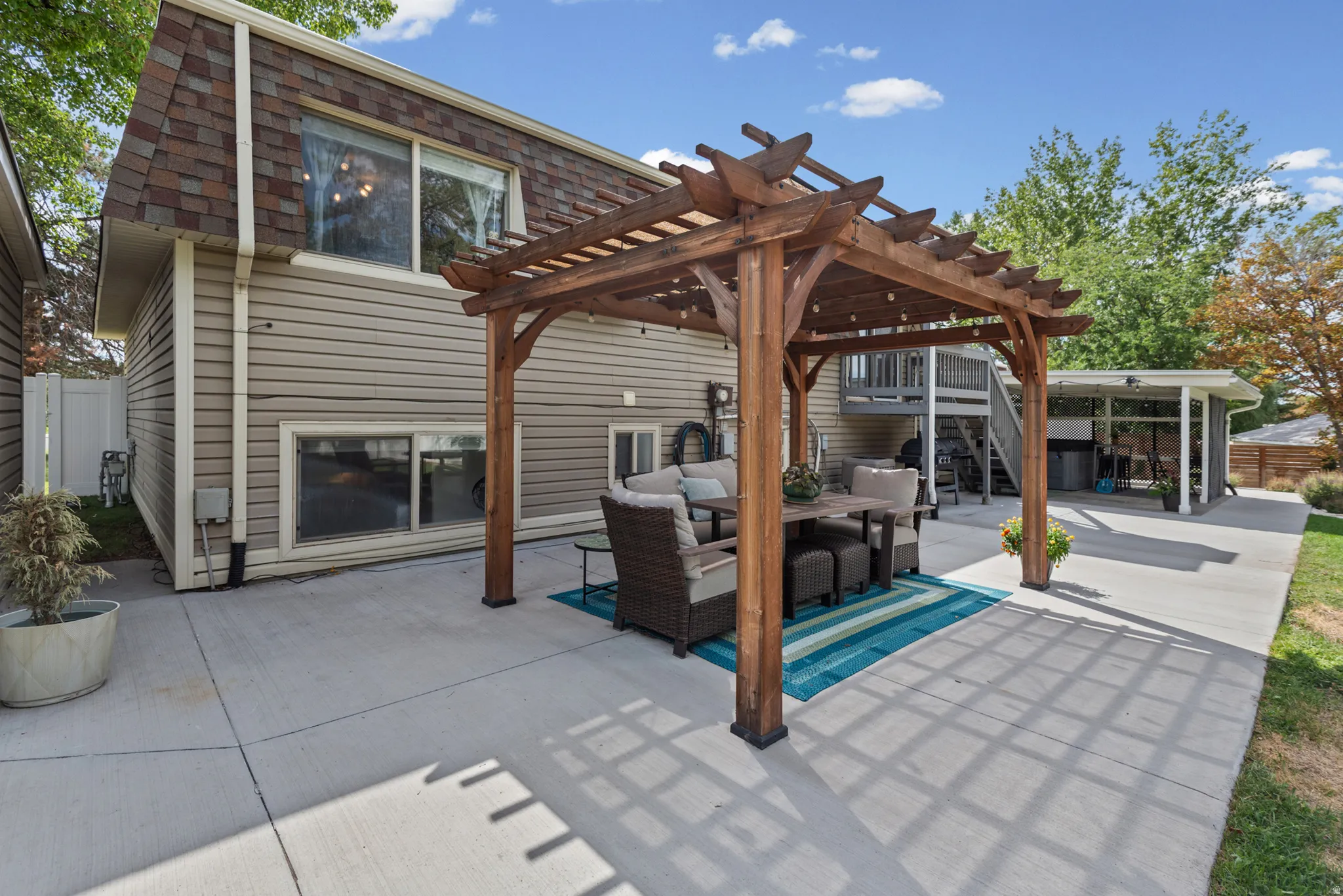 Expansive concrete patio featuring a wooden pergola, siding exterior, and an upper-level exterior staircase