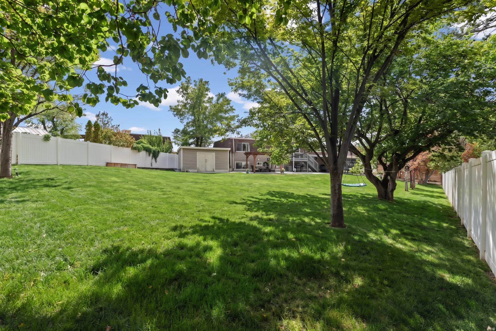 Expansive backyard featuring a manicured lawn, mature trees, a privacy fence, and a storage shed