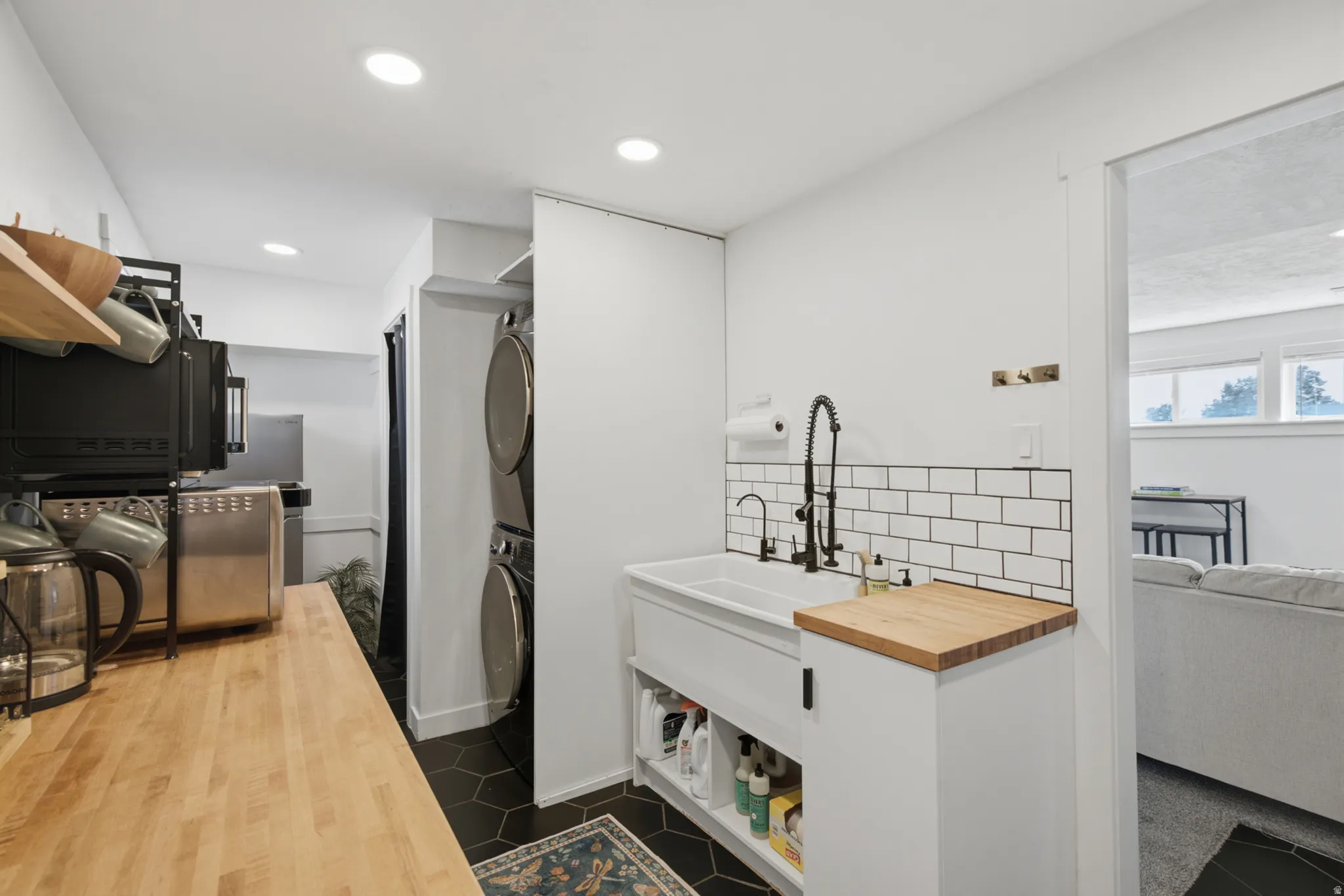 Hexagonal tile flooring, butcher block countertop, white subway tile backsplash, farmhouse-style sink, and built-in stacked laundry appliances