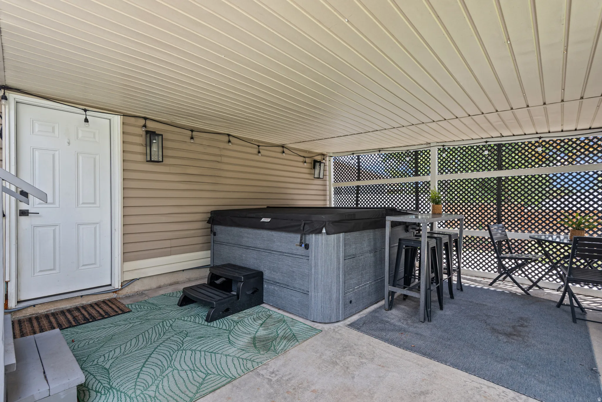 Covered patio featuring a spa, lattice privacy screening, and outdoor wall sconces