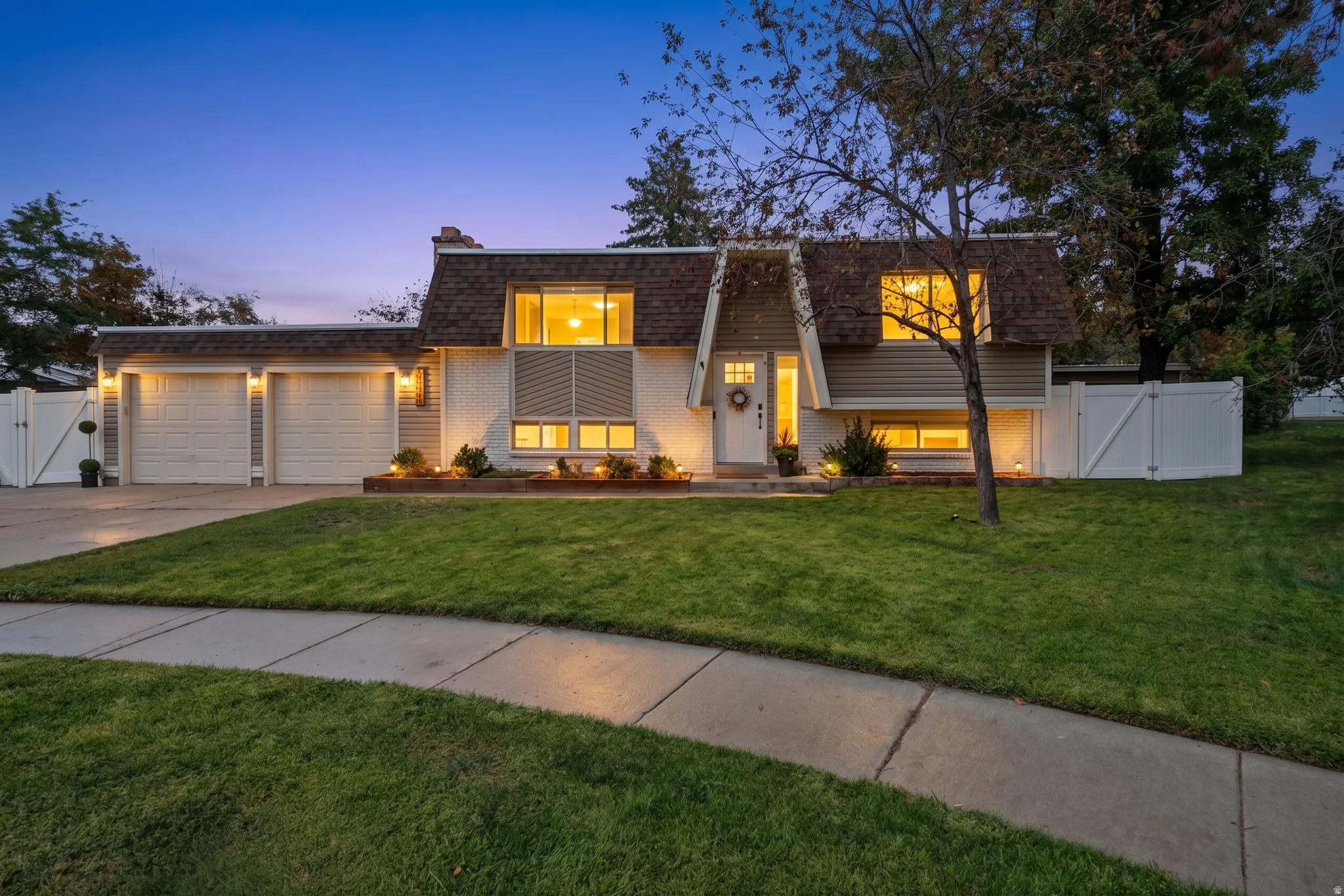 Split-level residence featuring a two-car garage, white picket fencing, and a manicured lawn