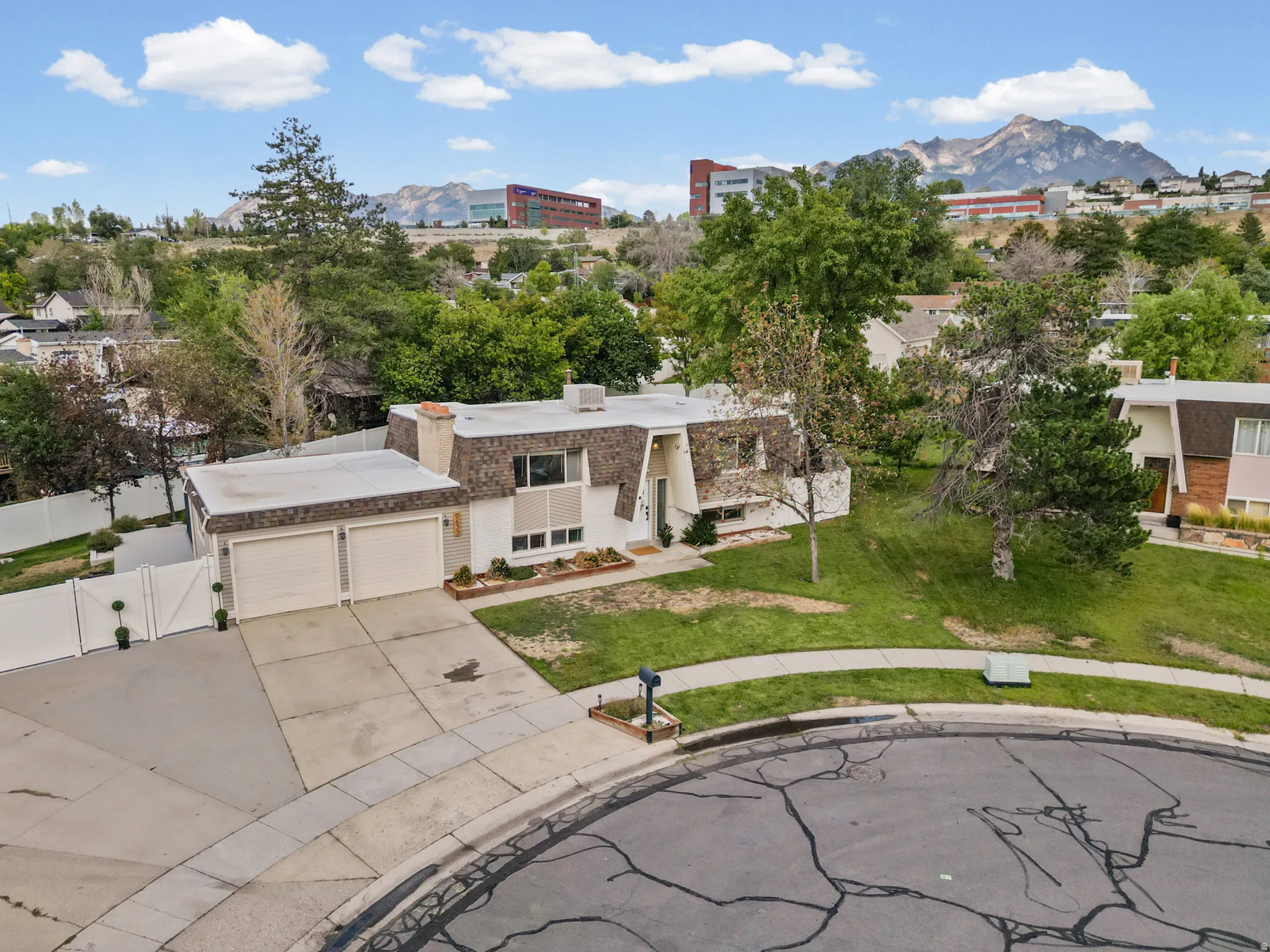 Two-car garage with concrete driveway, mature landscaping, and a sloped front lawn